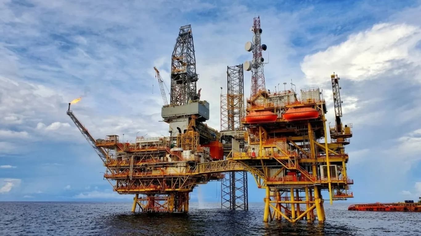 An offshore drilling platform with a derrick, cranes and orange lifeboats, standing in open sea